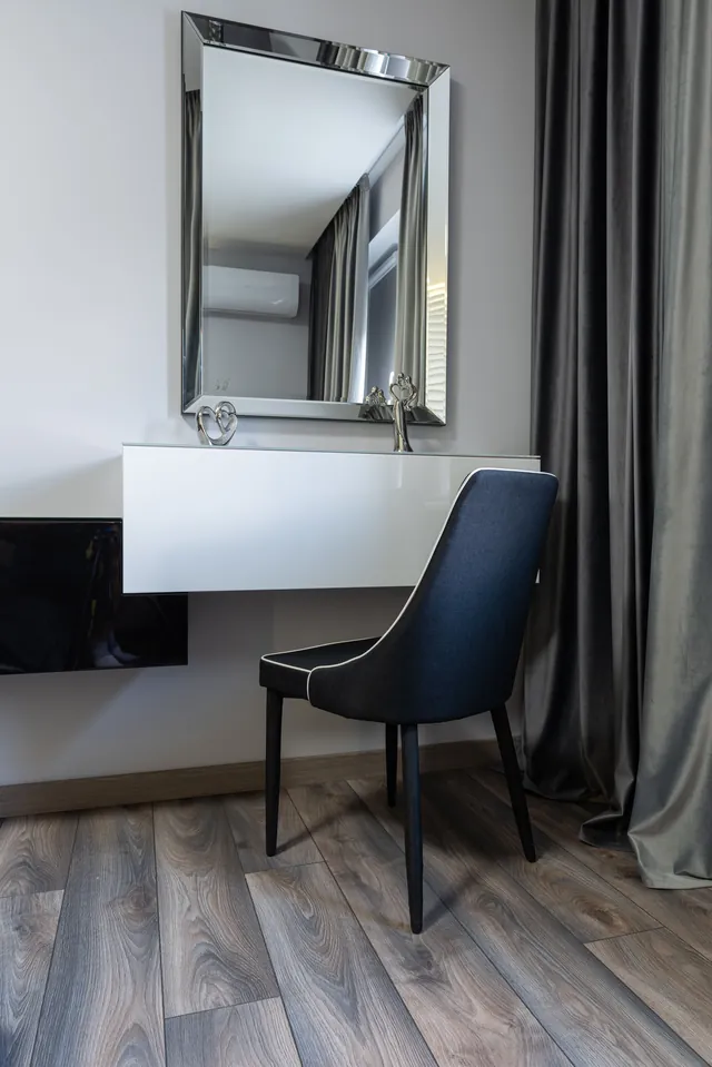 Glossy white wall-mounted floating dressing table beneath a bevelled wall mirror, with a dark upholstered chair
