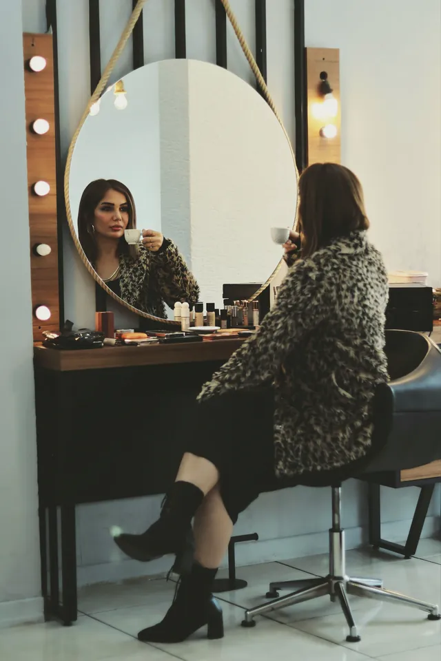 Makeup station with a wood-tone tabletop on a dark base, a large round mirror hung by rope and vertical bulb light panels on both sides