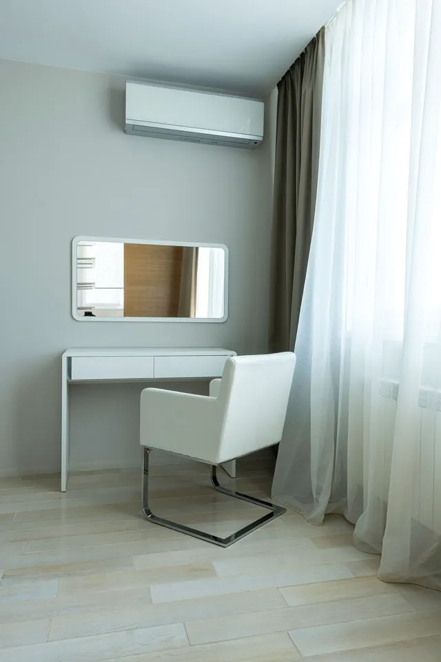 Minimal white dressing table with two drawers and panel legs beneath a rounded rectangular wall mirror, with a white armchair