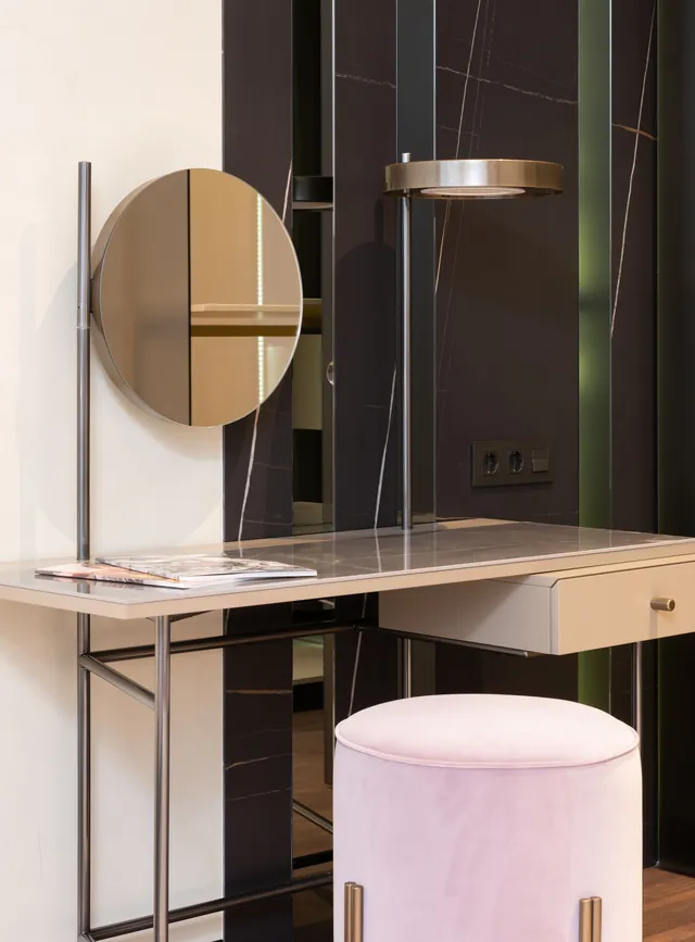 Slim metal-frame vanity table with a round mirror and ring-shaped lamp on upright rods, a stone-look tabletop and one drawer, with a pink velvet stool